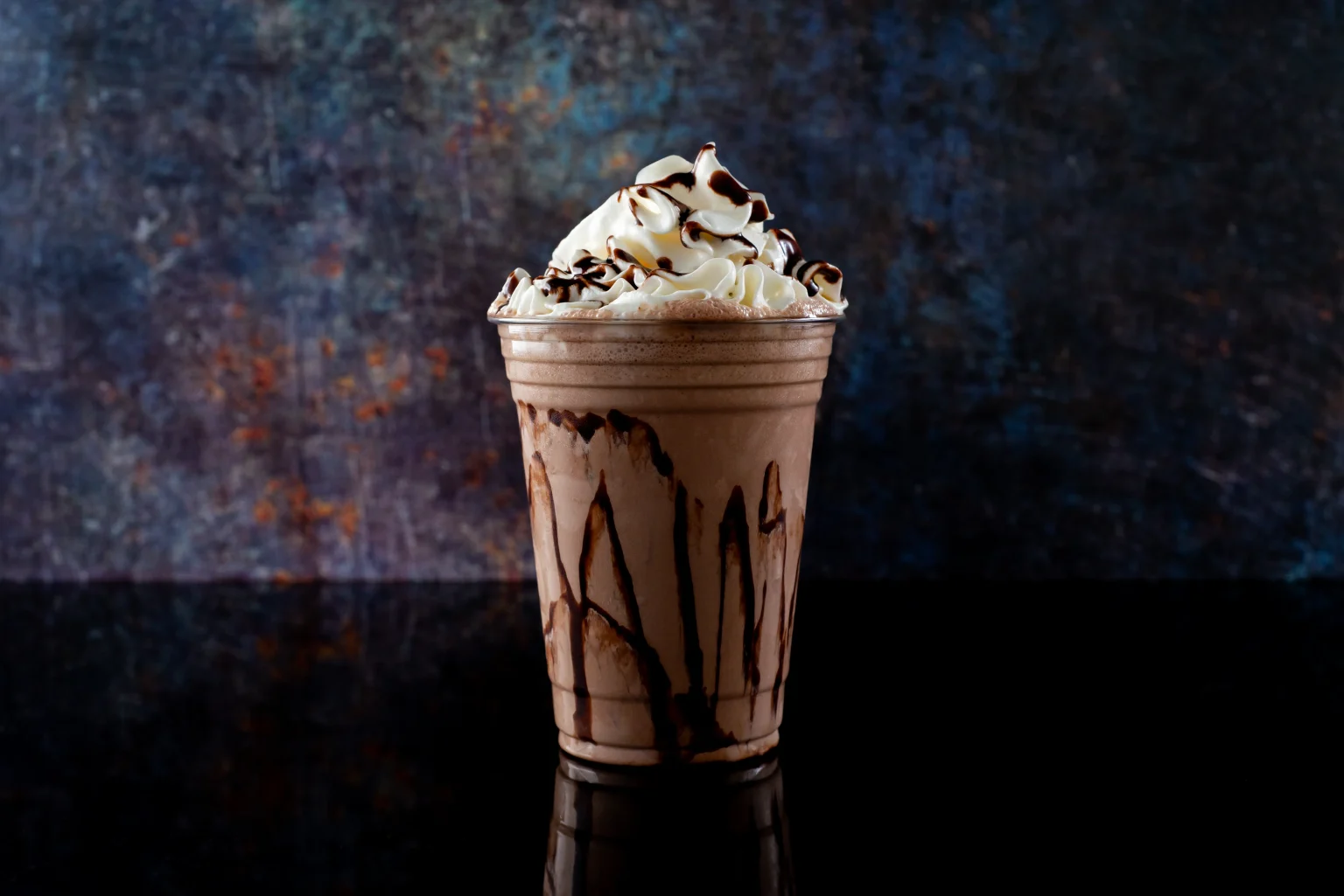Vaso con frappé de chocolate y abundante crema batida sobre fondo oscuro resaltando la textura del polvo para frappé fino.