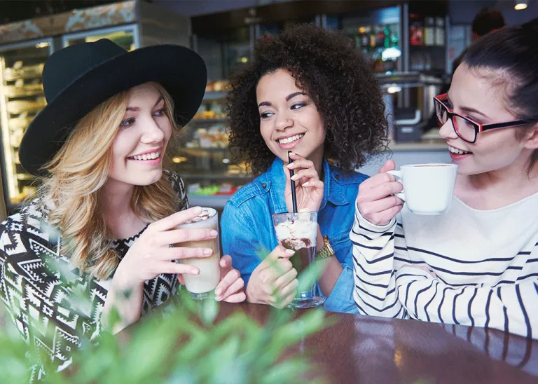 Tres mujeres jóvenes sonriendo y bebiendo café y malteadas hechas con insumos para cafetería de alta calidad profesional